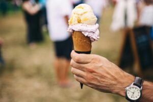Hand holding an ice cream cone with multiple flavors outdoors on a sunny day.