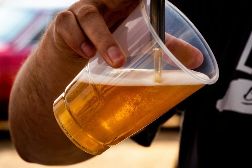 Close-up of a person pouring golden craft beer into a clear plastic cup.