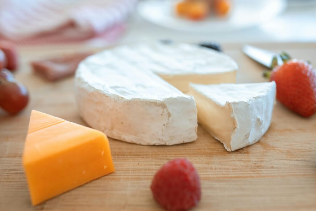 A wooden board featuring brie, cheddar cheese, and fresh fruits for tasting.